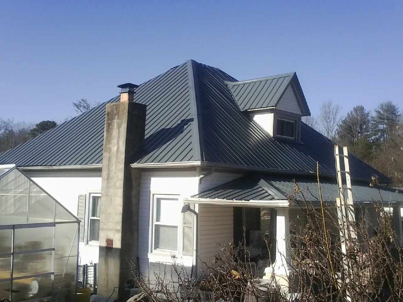 Dark blue standing seam metal roof on a white farmhouse with dormer — Slate & Tile Roof Repair by Roofing Brothers in Burtrum