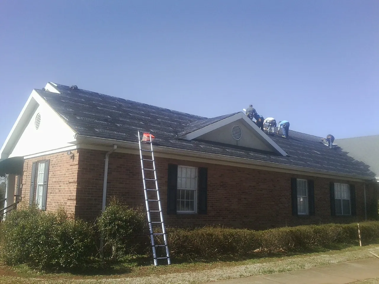 Crew tearing shingles off a brick ranch roof with a ladder set — Emergency Roof Repair work by our crew in Burtrum