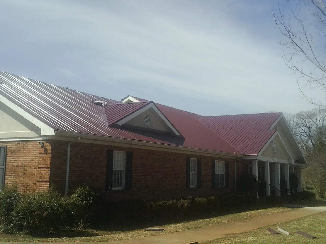 Red metal roof with gabled entries on a long brick building, from a Hail Damage Roof Repair job in Burtrum