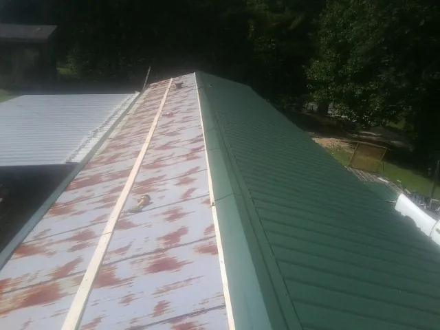 Old rusted panels beside newly installed green metal roofing — Wind Damage Roof Repair by Roofing Brothers in Burtrum