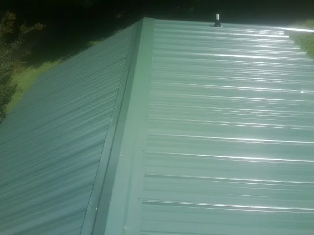 New green metal panels meeting at the ridge of a roof — Flat Roof Repair work by our crew in Burtrum