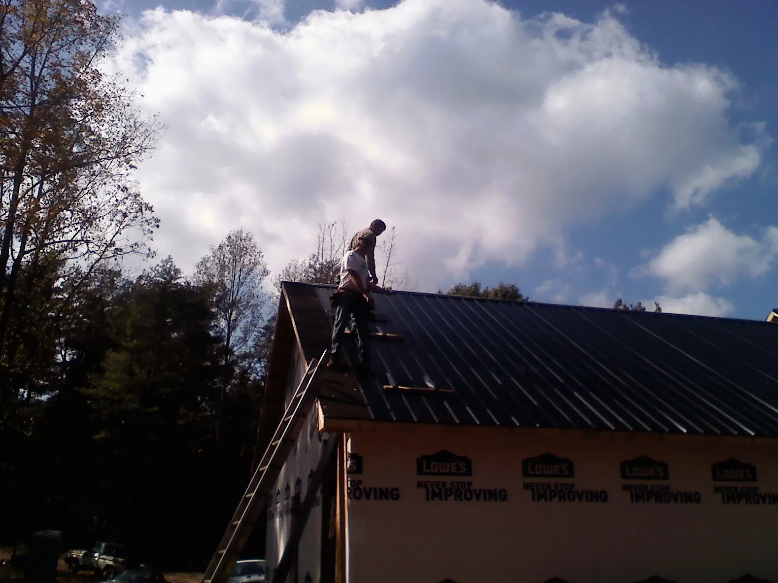 Roofer fastening dark metal panels high against a cloudy sky, from a Roof Inspection job in Burtrum