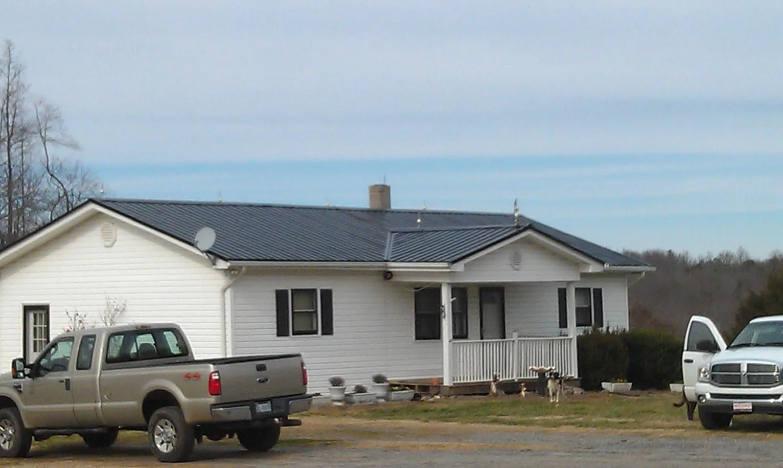 Finished dark metal roof on a white ranch home with work trucks parked in Burtrum