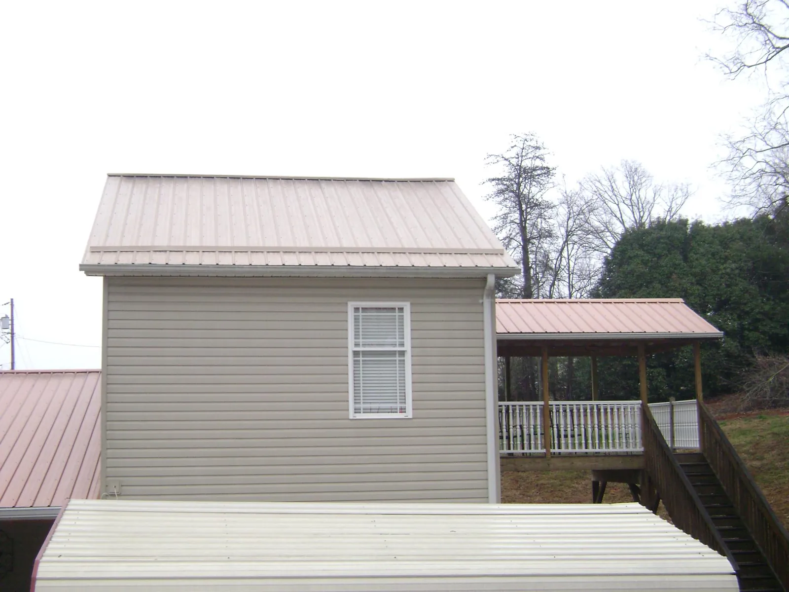 Tan metal roofs on a two story addition and attached porch, from a Roof Replacement job in Burtrum